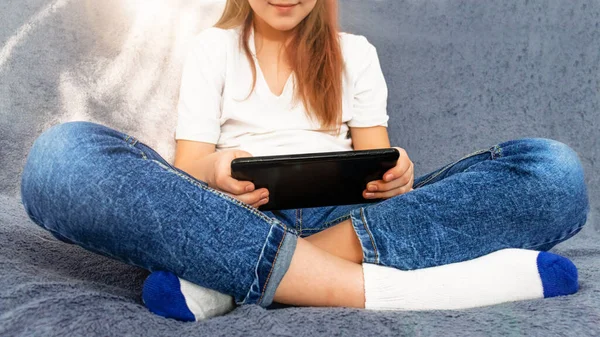 Genç kız tablet kullanır ve kanepeye oturur. Kişiliğini kaybetme. Teknolojiyi kullanan çocuklar. Aletlerle çocukluk.