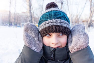 Erkek çocuk eldivenlerin arkasından bakar ve gülümser. Kış oyunları, çocuk eğlencesi.,