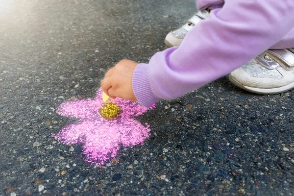 Kız çocuğu renkli tebeşirle kaldırıma pembe bir çiçek çizer. Çocukların elleri sarı tebeşiri tutar ve kaldırıma bir çiçek çizer.. 