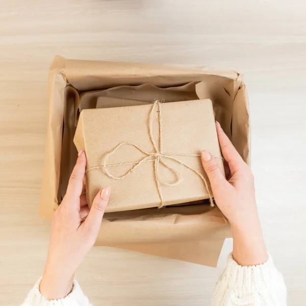 Kraft kağıdında paketleri olan ve sicimle bağlanmış bir kutuyu açıyorum. Ekolojik ambalaj, kağıt geri dönüşümü. Kraft kağıdı. Genç bir kadın evde bir paket açıyor. Yukarıdan bakıldığında, kadının elleri bir paket dolusu Kraft kağıdı tutuyor ve paketi evde açıyor.