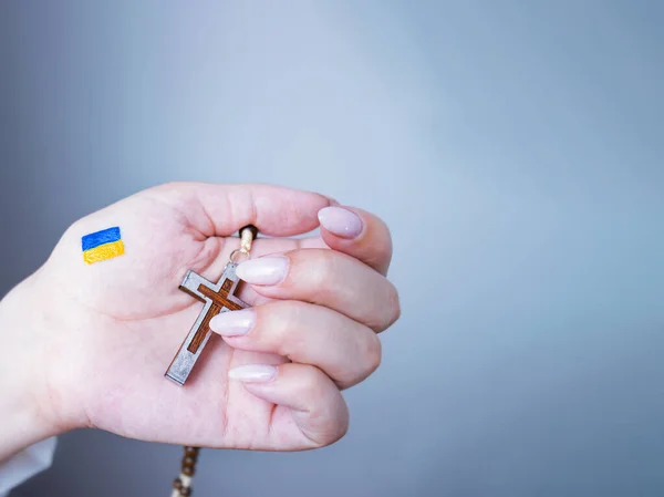 ukrainian flag painted on hand, prayer for peace,female hand with the image of the flag of ukraine holds a cross, 