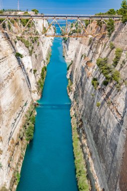 Sabah güneşi, yüksek ve sarp duvarlarla çerçevelenmiş Korint Kanalı 'nın mavi sularına yansıyor..