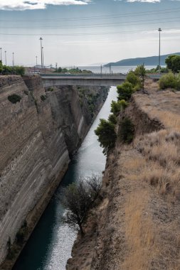 Sabah güneşi, yüksek ve sarp duvarlarla çerçevelenmiş Korint Kanalı 'nın mavi sularına yansıyor..