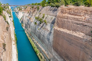 Sabah güneşi, yüksek ve sarp duvarlarla çerçevelenmiş Korint Kanalı 'nın mavi sularına yansıyor..