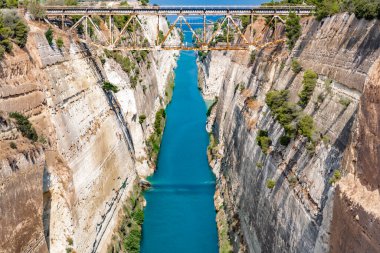 Sabah güneşi, yüksek ve sarp duvarlarla çerçevelenmiş Korint Kanalı 'nın mavi sularına yansıyor..
