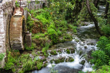 Yunanistan 'ın Livadia kentinde, paslı tekerleği olan eski bir su değirmeninin kalıntılarının yanında bir dağ deresi akıyor..