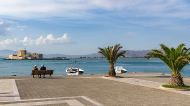 Yaşlı bir çift gecelerini Yunanistan 'ın Nafplion kentinin setinde eski kale manzaralı bir bankta geçirirler.