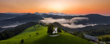 Skofja Loka, Slovenya - Sveti Tomaz 'ın (Aziz Thomas) güzel tepelik kilisesinin havadan panoramik manzarası ve yaz mevsiminde inanılmaz sisli gündoğumu ve Julian Alpleri