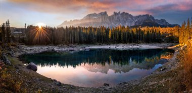 Carezza, İtalya - İtalyan Dolomitlerle birlikte Carezza Gölü 'nün (Lago di Carezza) panoramik manzarası gölü yansıtıyor. Güney Tyrol 'da ılık sonbahar gündoğumu, yükselen güneş ve renkli gökyüzü