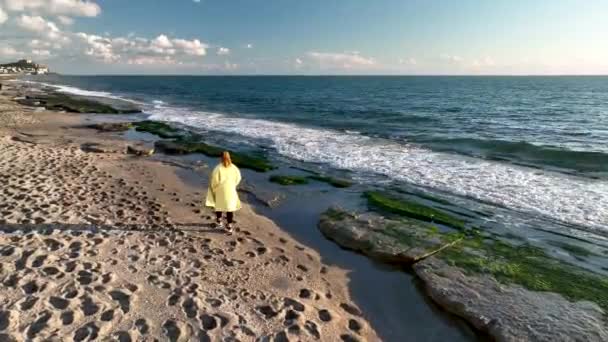 黄色のコートを着た女の子が海岸を歩いている — ストック動画