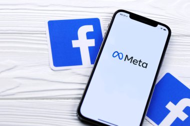 KHARKOV, UKRAINE - 29 Ekim 2021: Meta veya MetaVerse logosu olan Iphone 12 Pro, iki kağıttan Facebook logosu olan ahşap masa üzerinde bulunuyor.