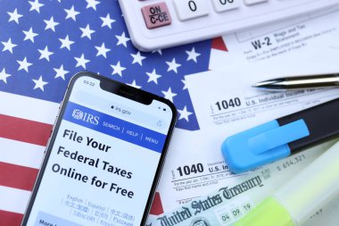 KHARKOV, UKRAINE - 5 Mart 2021: iPhone 12 'de resmi IRS web sitesi 1040 ve W-2 kağıt vergi formları ABD bayrağında