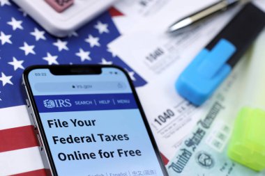 KHARKOV, UKRAINE - 5 Mart 2021: iPhone 12 'de resmi IRS web sitesi 1040 ve W-2 kağıt vergi formları ABD bayrağında