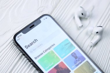 KHARKOV, UKRAINE - 5 Mart 2021: Apple müzik simgesi ve uygulaması iPhone 12 profosyonel ekranda beyaz ahşap masadaki uçak podları profosyoneli