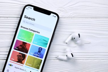 KHARKOV, UKRAINE - 5 Mart 2021: Apple müzik simgesi ve uygulaması iPhone 12 profosyonel ekranda beyaz ahşap masadaki uçak podları profosyoneli