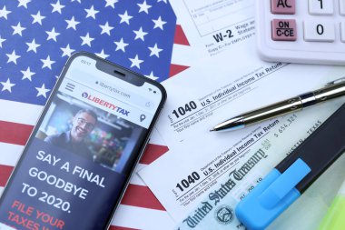 KHARKOV, UKRAINE - 5 Mart 2021: ABD bayrağında 1040 ve w-2 kağıt vergi formlarıyla birlikte iPhone 12 profesyonel ekranda LibertyVerx web sitesi