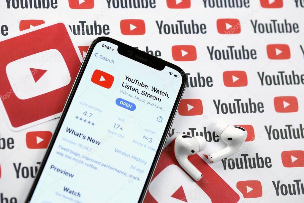 KHARKOV, UKRAINE - MARCH 5, 2021: Youtube icon and application from App store on iPhone 12 pro display screen with airpods pro on white wooden table
