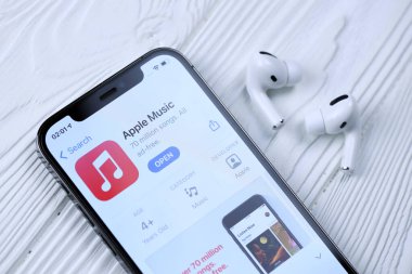 KHARKOV, UKRAINE - 5 Mart 2021: Apple müzik simgesi ve uygulaması iPhone 12 profosyonel ekranda beyaz ahşap masadaki uçak podları profosyoneli