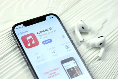 KHARKOV, UKRAINE - 5 Mart 2021: Apple müzik simgesi ve uygulaması iPhone 12 profosyonel ekranda beyaz ahşap masadaki uçak podları profosyoneli