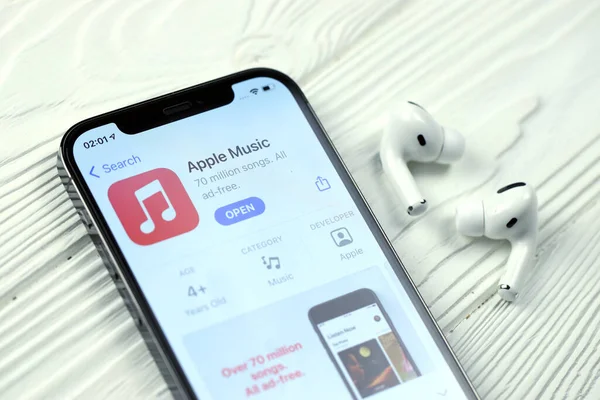 KHARKOV, UKRAINE - 5 Mart 2021: Apple müzik simgesi ve uygulaması iPhone 12 profosyonel ekranda beyaz ahşap masadaki uçak podları profosyoneli