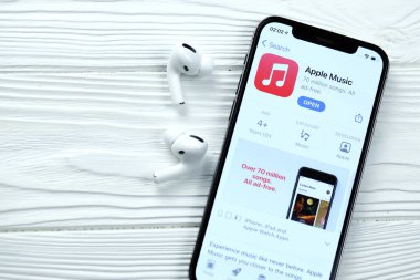 KHARKOV, UKRAINE - 5 Mart 2021: Apple müzik simgesi ve uygulaması iPhone 12 profosyonel ekranda beyaz ahşap masadaki uçak podları profosyoneli