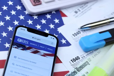 KHARKOV, UKRAINE - 5 Mart 2021: iPhone 12 'de resmi IRS web sitesi 1040 ve W-2 kağıt vergi formları ABD bayrağında