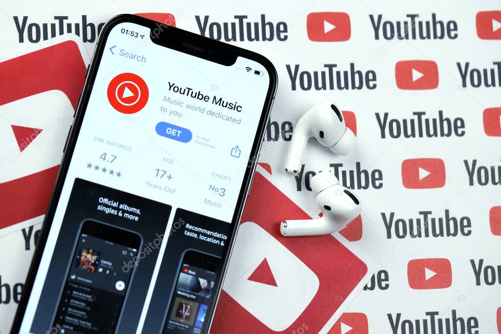 KHARKOV, UKRAINE - MARCH 5, 2021: Youtube music icon and application from App store on iPhone 12 pro display screen with airpods pro on white wooden table
