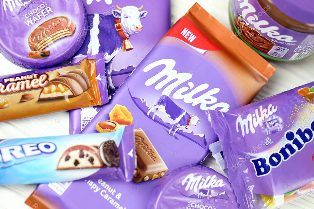 KHARKOV, UKRAINE - JULY 2, 2021: Milka chocolate products with classical lilac color wrapping design on white wooden table