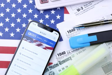 KHARKOV, UKRAINE - 5 Mart 2021: iPhone 12 'de resmi IRS web sitesi 1040 ve W-2 kağıt vergi formları ABD bayrağında