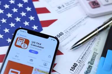 KHARKOV, UKRAINE - 5 Mart 2021: ABD Vergi Hesap Makinesi uygulaması iPhone 12 profesyonel ekranda 1040 ve W-2 kağıt vergi formları ABD bayrağında
