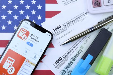 KHARKOV, UKRAINE - 5 Mart 2021: ABD Vergi Hesap Makinesi uygulaması iPhone 12 profesyonel ekranda 1040 ve W-2 kağıt vergi formları ABD bayrağında