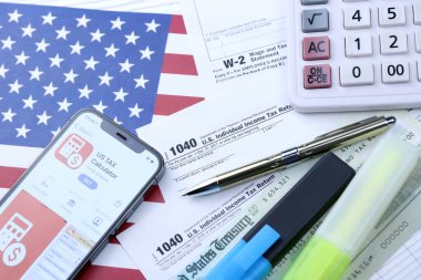 KHARKOV, UKRAINE - 5 Mart 2021: ABD Vergi Hesap Makinesi uygulaması iPhone 12 profesyonel ekranda 1040 ve W-2 kağıt vergi formları ABD bayrağında