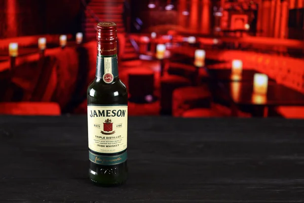 Kharkov Ukraine 2021年2月14日 Jameson在木制桌子上的三蒸馏水爱尔兰威士忌瓶 背景为红色条状内部 精英酒精生产 — 图库照片