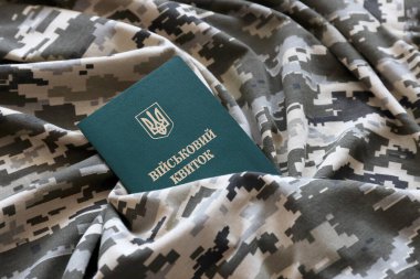 Piksel kamuflaj dokusuna sahip kumaş üzerinde Ukrayna askeri kimliği. Gri, kahverengi ve yeşil pikselli kamuflaj desenli kumaş Ukrayna ordusunun kişisel jetonuyla yakın plan..