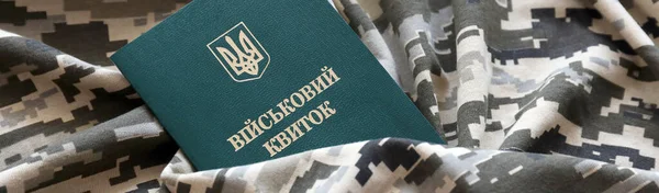 Ukrainian military ID on fabric with texture of pixeled camouflage. Cloth with camo pattern in grey, brown and green pixel shapes with Ukrainian army personal token close up.