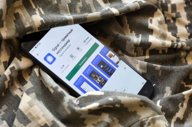 TERNOPIL, UKRAINE - APRIL 24, 2022: Signal Private Messenger app play store page on the display of a black mobile smartphone on ukrainian military camouflage uniform