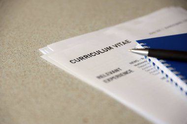 Top view of stack of office documents including resume and cv forms on the desk close to pen and notepad. Job seeking process. Hunting for workplace concept
