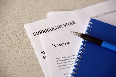 Top view of stack of office documents including resume and cv forms on the desk close to pen and notepad. Job seeking process. Hunting for workplace concept