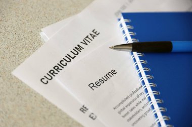 Top view of stack of office documents including resume and cv forms on the desk close to pen and notepad. Job seeking process. Hunting for workplace concept