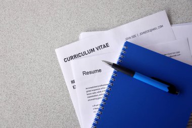 Top view of stack of office documents including resume and cv forms on the desk close to pen and notepad. Job seeking process. Hunting for workplace concept