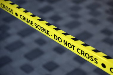 Crime scene tape for covering the area cordon. Yellow tape with blurred forensic law enforcement background in cinematic tone and copy space