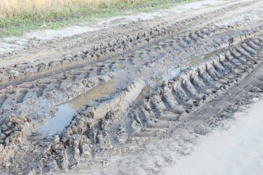 Kıvrımlı bir yolu olan sonbahar manzarası üzerinde tarımsal makinelerin büyük tekerleklerinin izleri görülebilir.