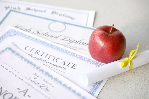 A honor roll recognition, certificate of achievement and high school diploma lies on table with small scroll and red apple. Education documents close up