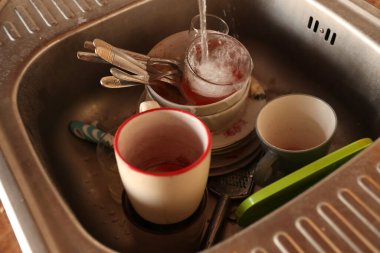 Mutfak lavabosunda yemek artıklarıyla dolu bir yığın kirli bulaşık. Yıkanmamış bulaşıklar temizlemeye hazır.