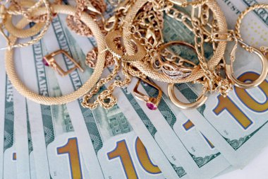Birçok pahalı altın mücevher yüzük, küpeler ve beyaz arka planda büyük miktarda Amerikan doları banknotları olan kolyeler. Rehinci ya da kuyumcu konsepti.