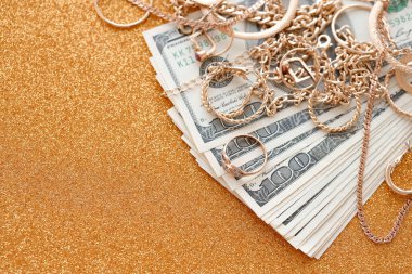 Many expensive golden jewerly rings, earrings and necklaces with big amount of US dollar bills on luxury glitter golden background surface. Pawnshop or jewerly shop concept