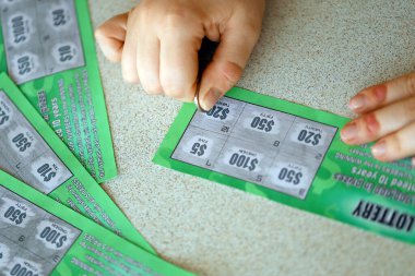 Close up view of silver coin in hand of gambler scratching fake lottery card. Lottery gambling concept, scratching cards lottery type