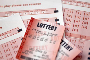 Red lottery ticket lies on pink gambling sheets with numbers for marking to play lottery. Lottery playing concept or gambling addiction. Close up photo