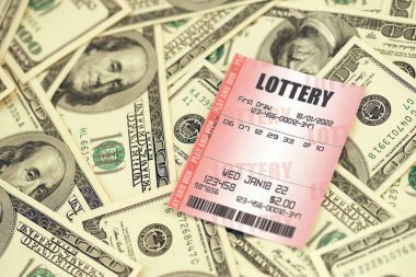 Red lottery ticket lies on big amount of hundred dollar bills. Lottery playing concept or gambling addiction. Close up photo