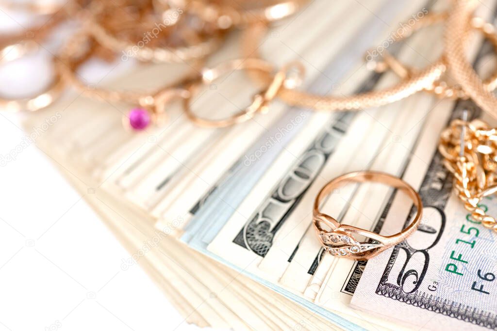 Many expensive golden jewerly rings, earrings and necklaces with big amount of US dollar bills on white background. Pawnshop or jewerly shop concept